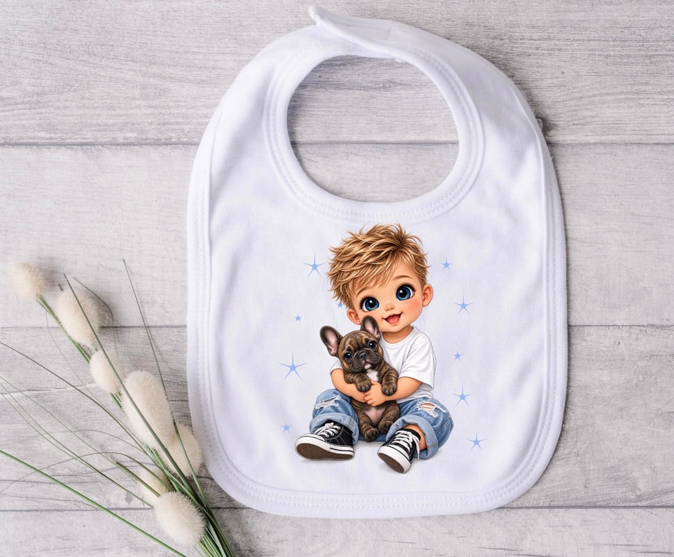 A white baby bib with a custom cartoon illustration of a blond boy hugging a small brown French bulldog, displayed on a light gray wood background next to decorative cotton stems.