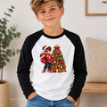 A young boy wearing a black and white raglan baseball t-shirt with a colorful Christmas graphic on the front, standing in a brightly lit indoor room.