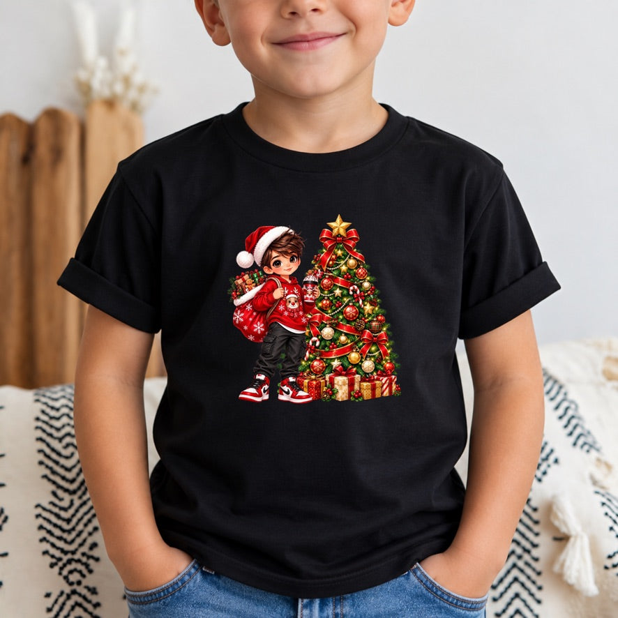 A child wearing a black short-sleeve t-shirt with a colorful cartoon graphic of a boy in a Santa hat next to a decorated Christmas tree. The child is sitting indoors on a patterned blanket.