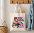A cream canvas tote bag hanging on a wall hook, decorated with a colorful cartoon graphic of a woman surrounded by shopping bags and the text 'Things I Didn't Do: Shop For'. A denim jacket hangs on the right, a woven basket is on the left, and a wooden coat rack is above.