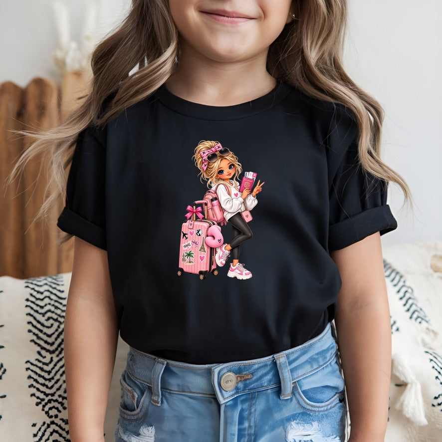 A young girl wearing a black short-sleeve t-shirt with a colorful cartoon graphic of a girl with pink luggage and a drink, paired with blue jeans.