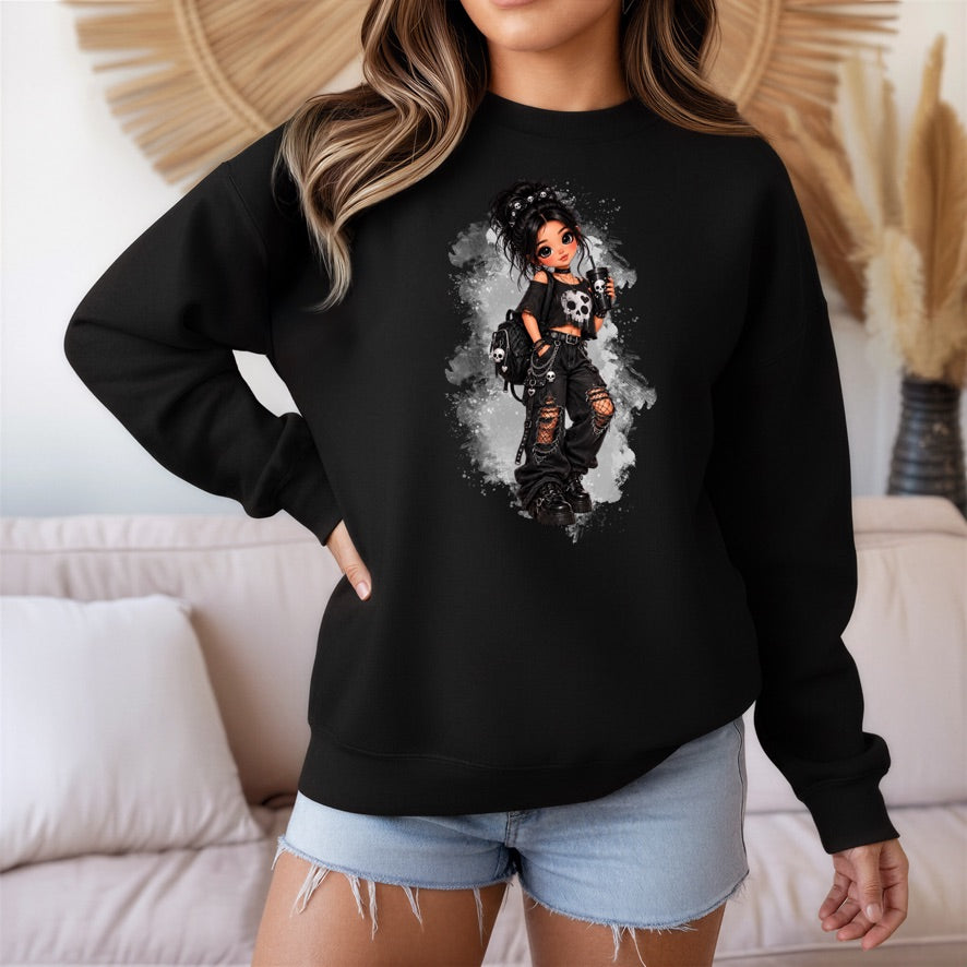 A woman wearing a black crewneck sweatshirt with a detailed graphic of a gothic anime-style girl holding a skull guitar, paired with light blue denim shorts in a cozy living room setting.