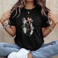 A woman wearing a black short-sleeve graphic t-shirt with a detailed illustration of a gothic anime-style girl in a black and white outfit, paired with light blue jeans and white sneakers.