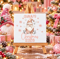 Personalised first Christmas ceramic tile with name and year, featuring a blush pink festive gnome and snowflakes displayed on a wooden stand.