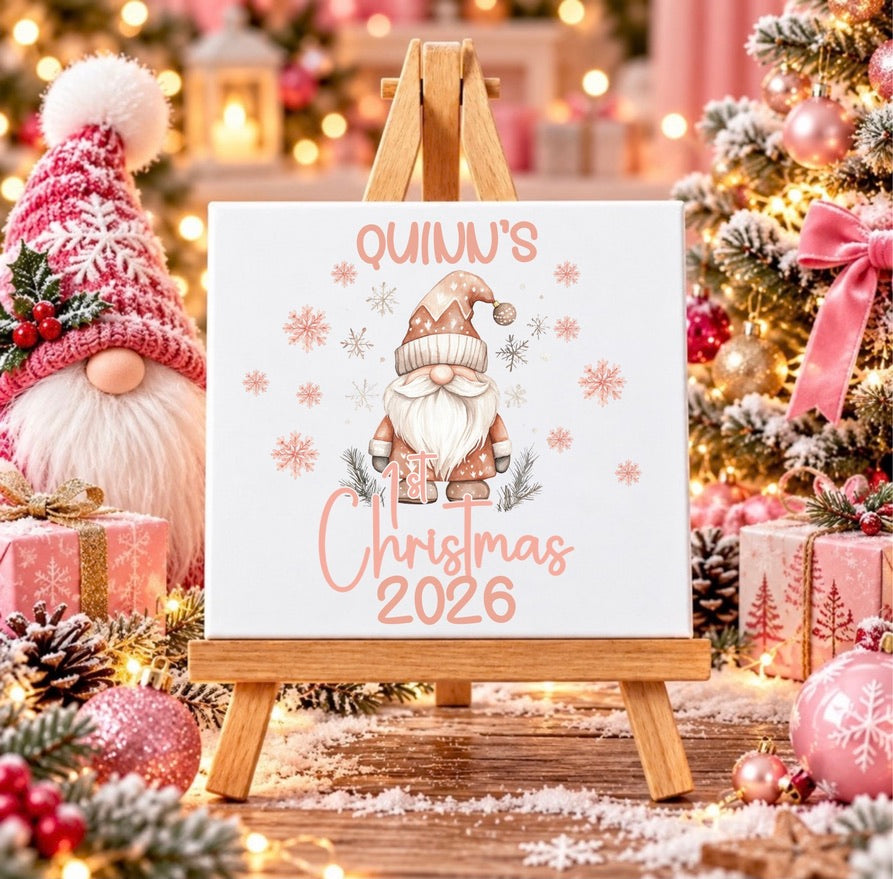 Personalised first Christmas ceramic tile with name and year, featuring a blush pink festive gnome and snowflakes displayed on a wooden stand.