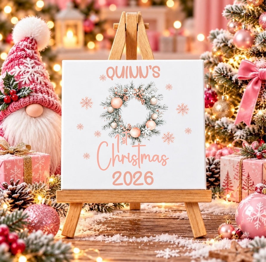 Personalised first Christmas ceramic tile with name and year, featuring a blush pink festive wreath and snowflakes displayed on a wooden stand.