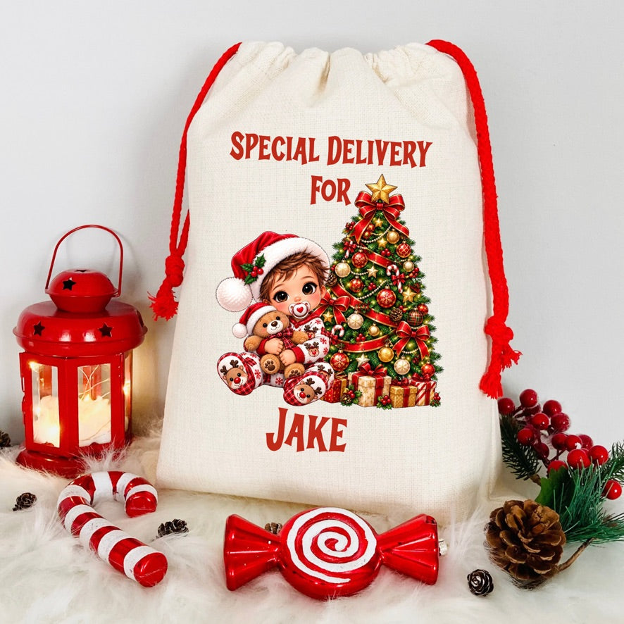 A cream-colored fabric Christmas gift sack with red drawstrings, printed with 'SPECIAL DELIVERY FOR JAKE' and a festive illustration of a child and a decorated Christmas tree. The sack is styled on a white faux-fur surface with red holiday props including a lantern, candy canes, a lollipop-shaped ornament, pinecones, and berry sprigs.