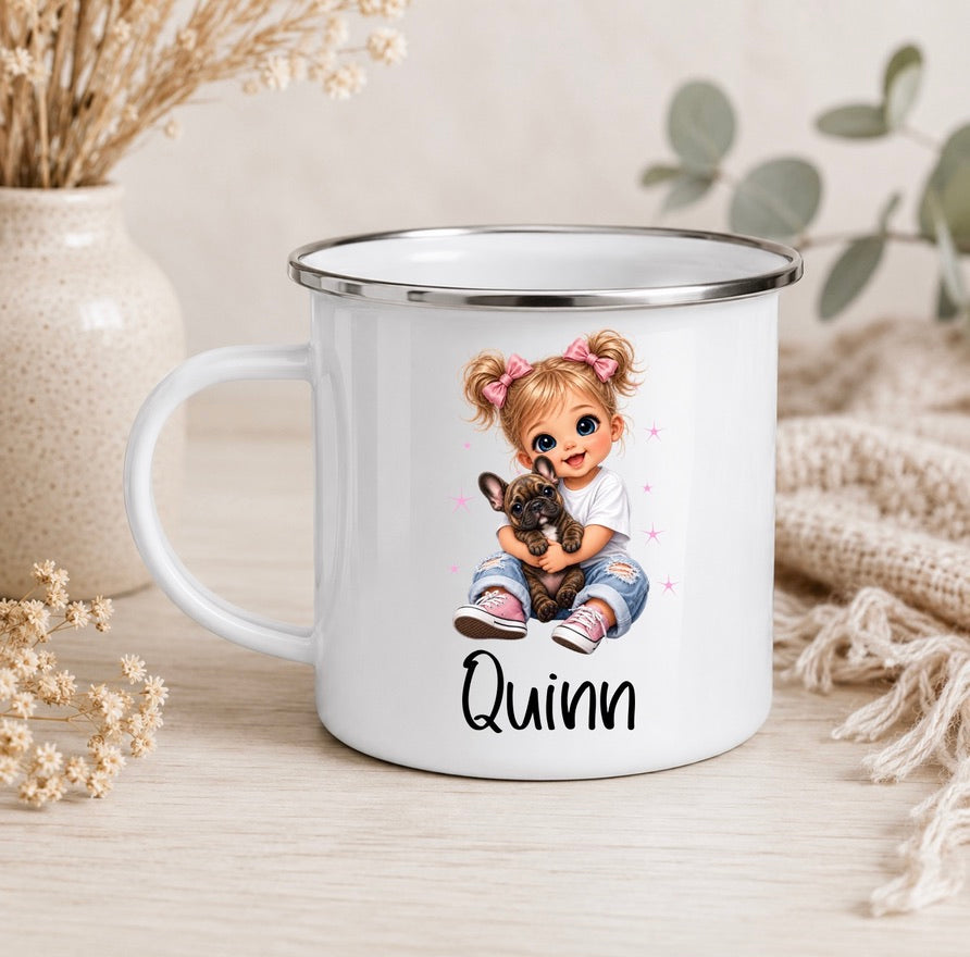 A white enamel-style mug with a silver rim, featuring a printed illustration of a girl with pigtails holding a dog and the name 'Quinn' below. The mug is styled on a light wood surface with dried flowers, a vase, and a knitted textile in the background.
