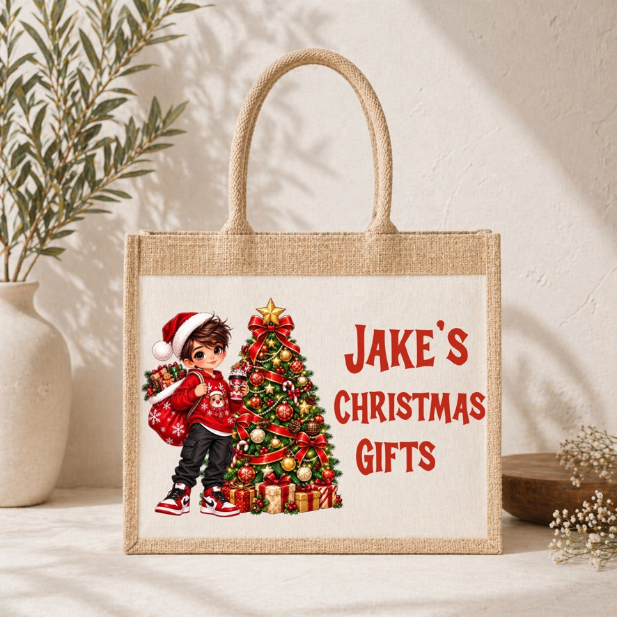 A natural jute tote bag with a printed Christmas illustration and the text 'Jake's Christmas Gifts' in red, styled on a tabletop with a plant and dried flowers in the background.