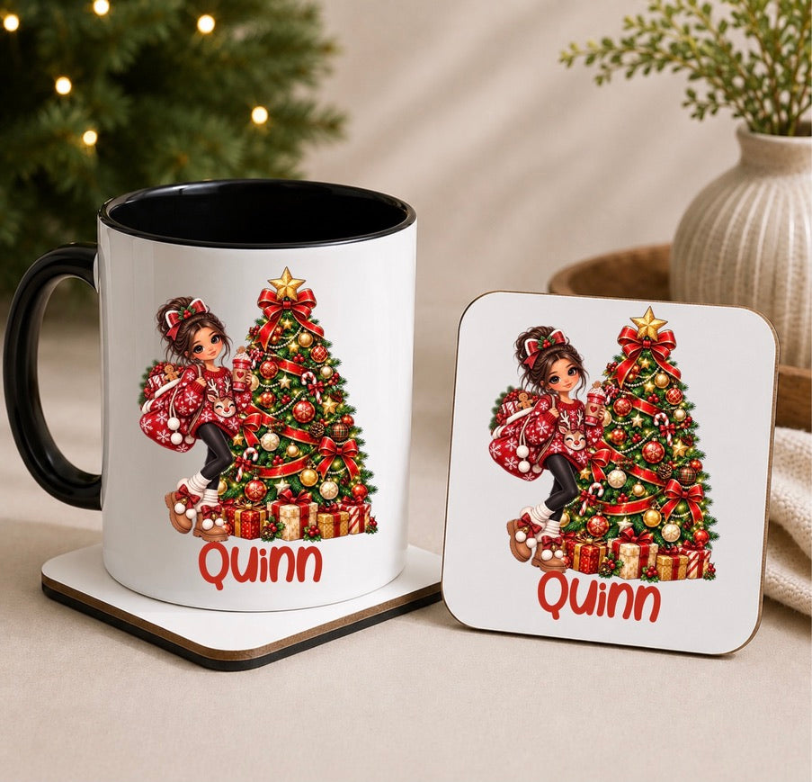 A white ceramic mug with a black handle and interior, alongside a matching square coaster, both printed with a festive Christmas tree illustration and the name 'Quinn' in red. The scene is styled on a beige surface with blurred holiday lights and a plant in the background.