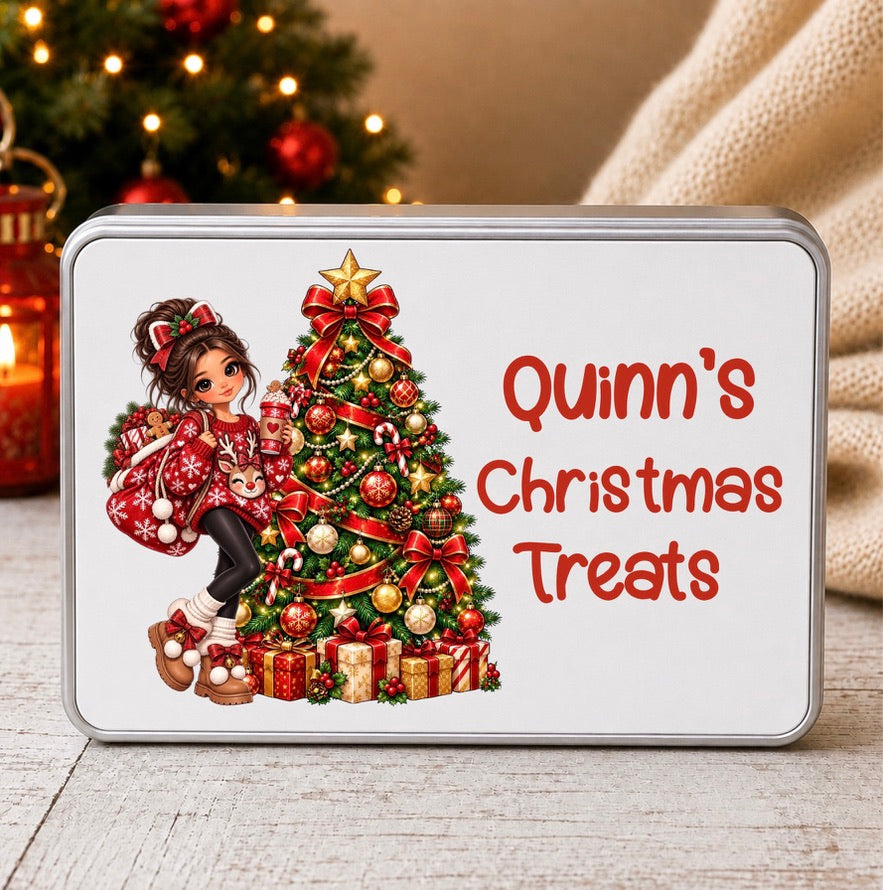 A rectangular metal tin with rounded corners sits on a light wood surface. The tin has a printed Christmas design featuring a girl in a red patterned coat beside a decorated Christmas tree, with the text 'Quinn's Christmas Treats' in red.