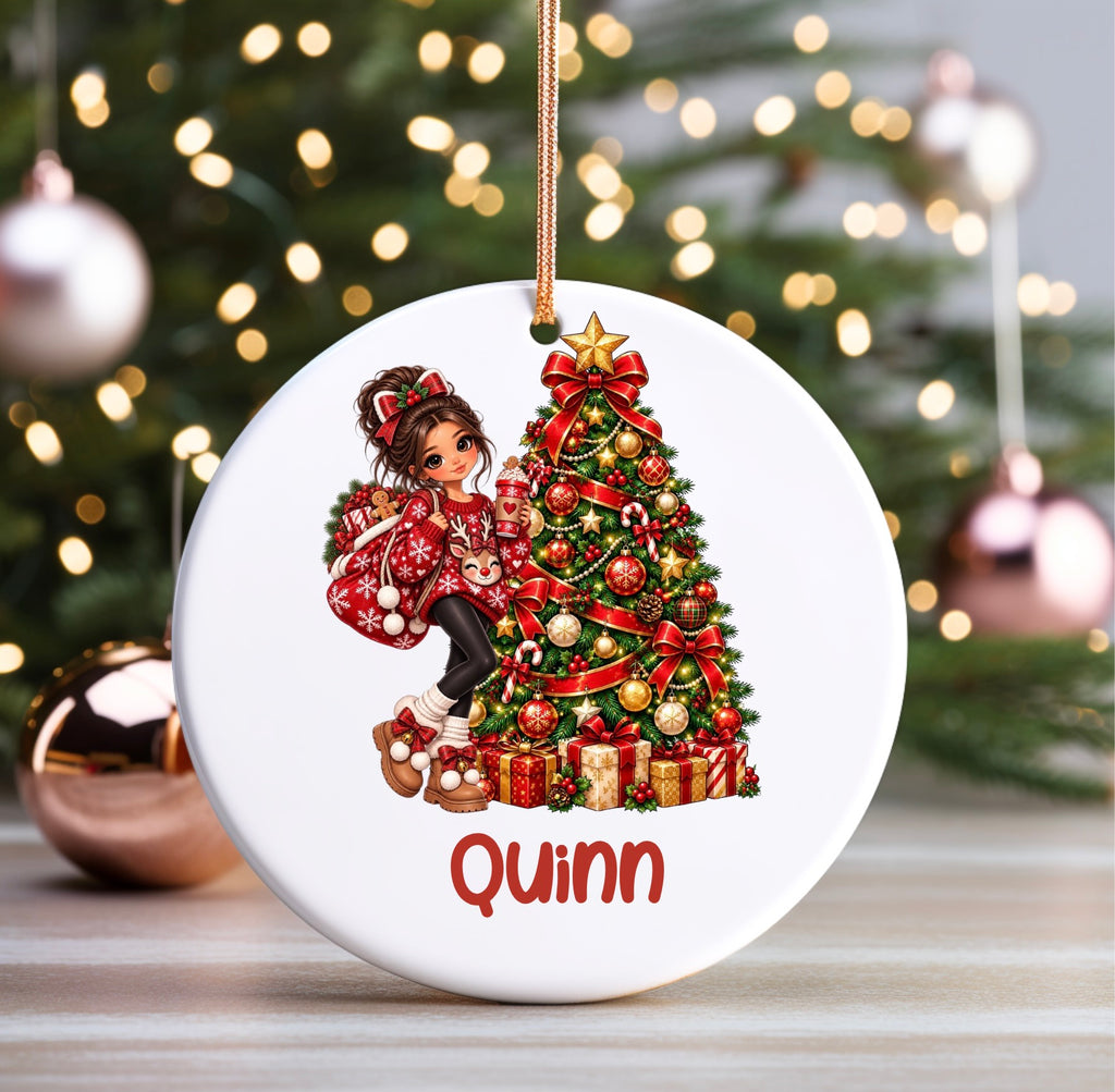 A personalized round white Christmas ornament featuring an illustration of a girl in a red patterned coat climbing a decorated Christmas tree, with the name 'Quinn' printed in red at the bottom. The ornament hangs from a gold string against a blurred festive background with lights and ornaments.