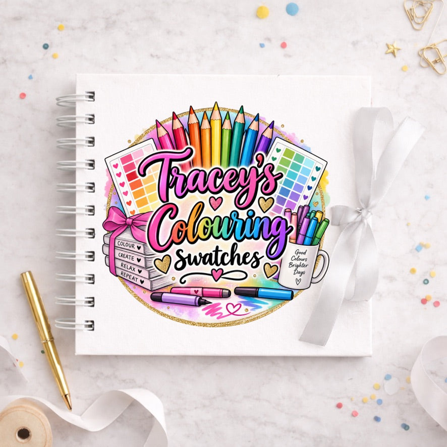 A white spiral-bound notebook with a colorful custom illustration reading 'Tracey's Colouring Swatches' on the cover, styled on a light marble surface with a gold pen, white ribbon, and small confetti.