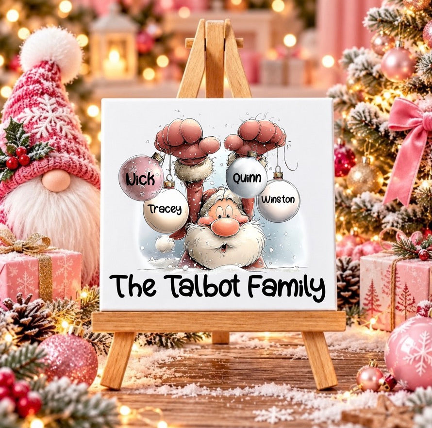 A custom tile featuring a festive Christmas illustration of Santa Claus surrounded by ornaments, displayed on a wooden easel. The canvas includes personalized names: 'Wick', 'Tracey', 'Quinn', and 'Winston' in round ornaments, with the text 'The Talbot Family' written at the bottom.