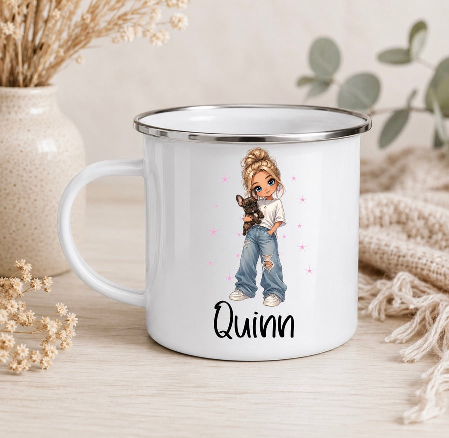 A white enamel-style mug with a silver rim sits on a light wood surface. The mug is printed with an illustration of a girl with blonde hair holding a small black dog, with pink stars and the name 'Quinn' in black script below.