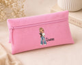 A pink canvas zipper pouch with a cartoon girl illustration and the name 'Quinn' printed on the front, styled on a beige surface with dried flowers and a book in the background.