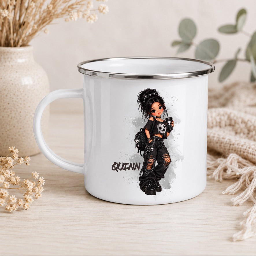 A white enamel-style mug with a silver rim sits on a light wood surface. The mug features a printed illustration of a gothic-style girl with the name 'QUINN' below her.