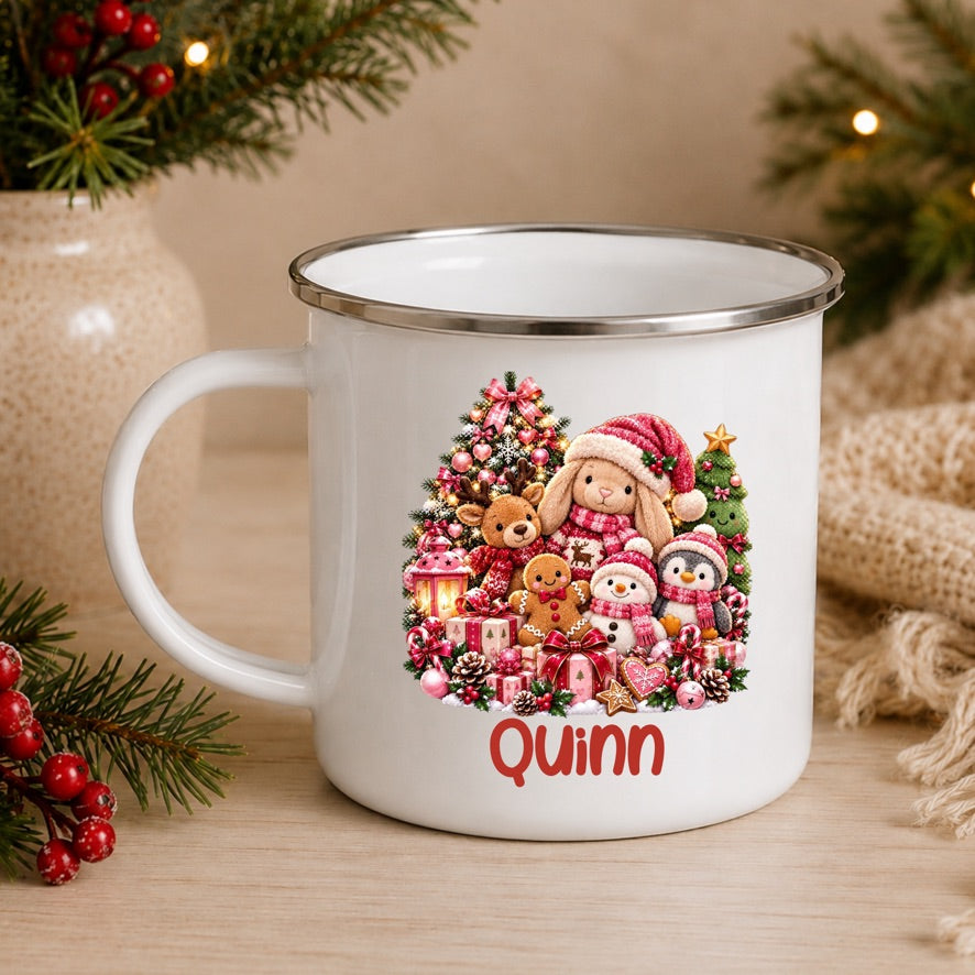 A white enamel-style mug with a silver rim, decorated with a festive Christmas teddy bear illustration and the name 'Quinn' in red script. The mug is styled on a wooden surface with holiday greenery, red berries, and a burlap sack in the background.