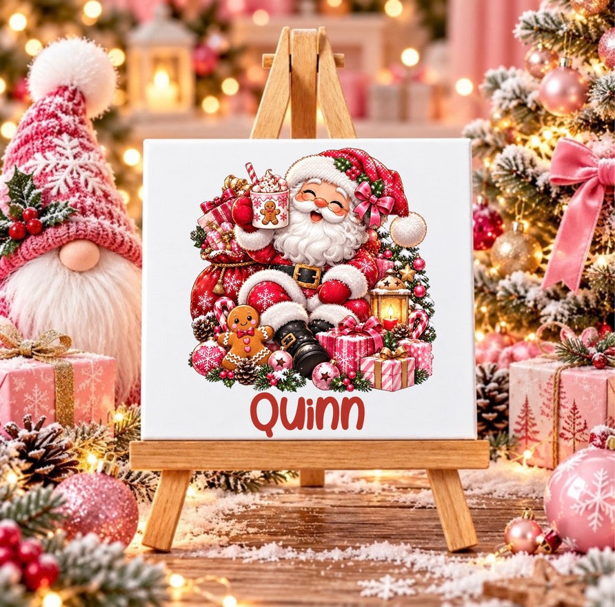 Personalised pink Santa Christmas ceramic tile with custom name, featuring Santa with hot chocolate, gingerbread and presents on a wooden display stand.
