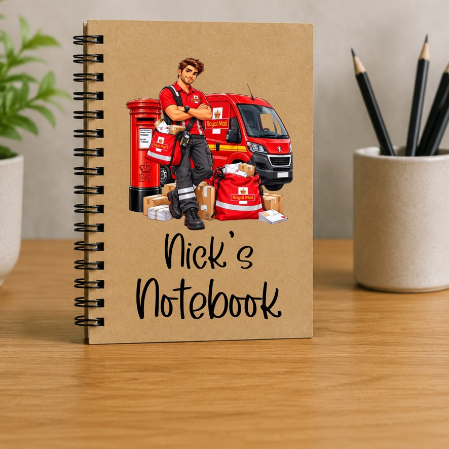 A spiral-bound notebook standing upright on a wooden desk. The notebook cover is kraft brown and features an illustration of a postal worker in a red uniform standing beside a red van and mail bags, with the text 'Nick's Notebook' written in black script.