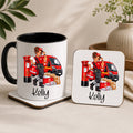 A white ceramic mug with a black handle and interior, alongside a matching square coaster, both printed with a personalized illustration of a postman in red uniform next to a red post box and van, with the name 'Kelly' in black script. The scene is styled on a beige surface with soft background props including a vase and leaves.