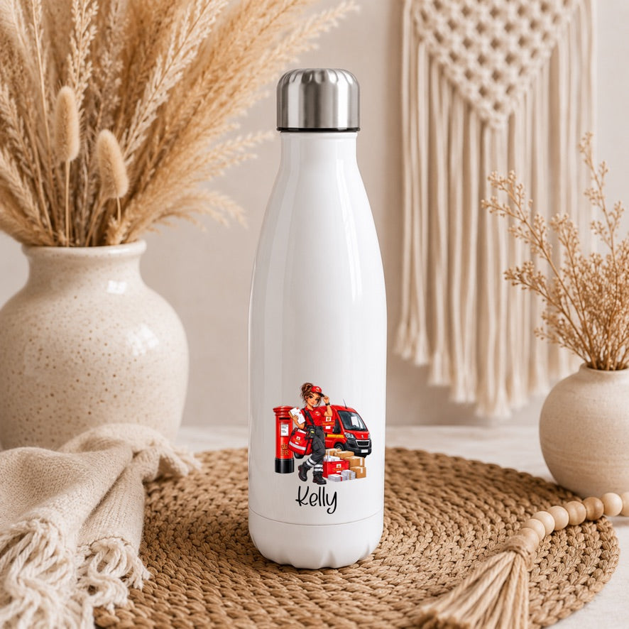 A white insulated water bottle with a silver cap stands on a woven mat in a styled indoor setting. The bottle has a printed illustration of a firefighter in red gear next to a red fire truck, with the name 'Kelly' written below in black script.