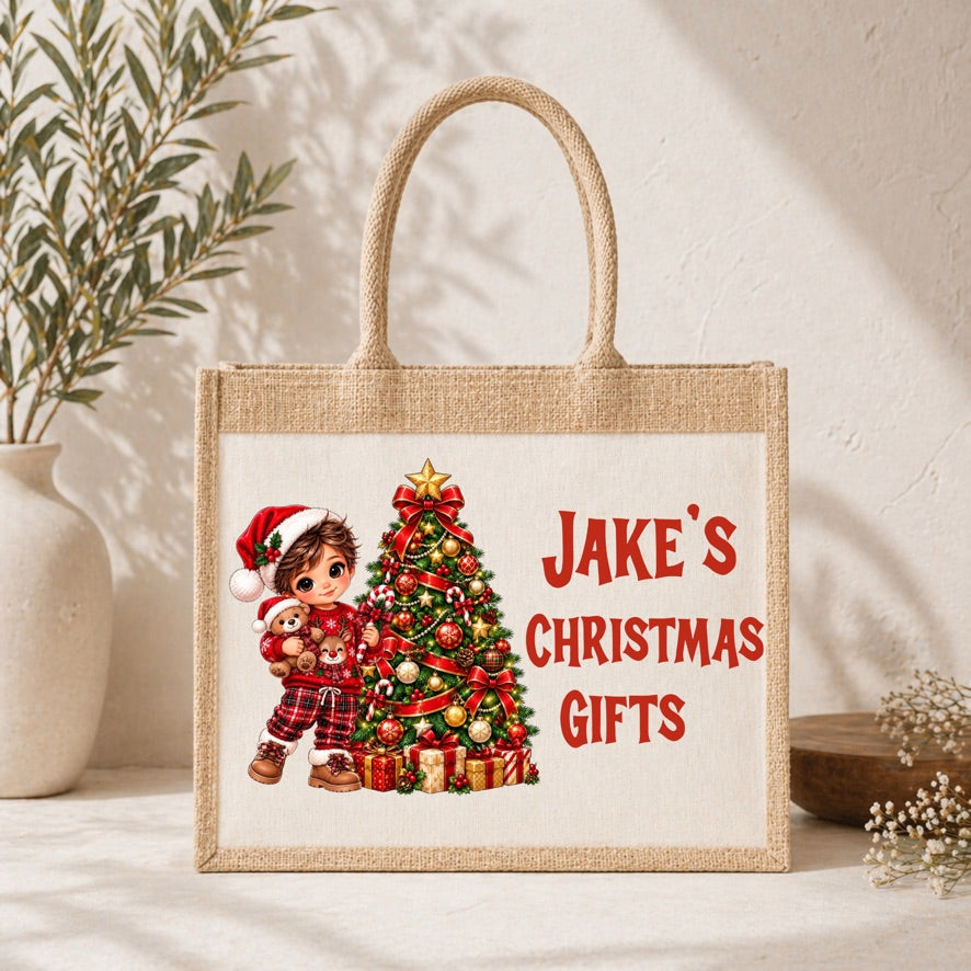 A natural jute tote bag with a printed Christmas illustration and the text 'Jake's Christmas Gifts' in red, styled on a light beige surface with decorative plants in the background.