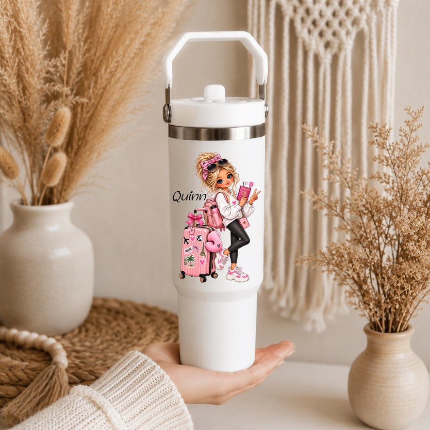A white insulated travel tumbler with a lid and carry handle, held in a hand. The tumbler features a colorful illustration of a girl with pink luggage and the text 'Queen'.