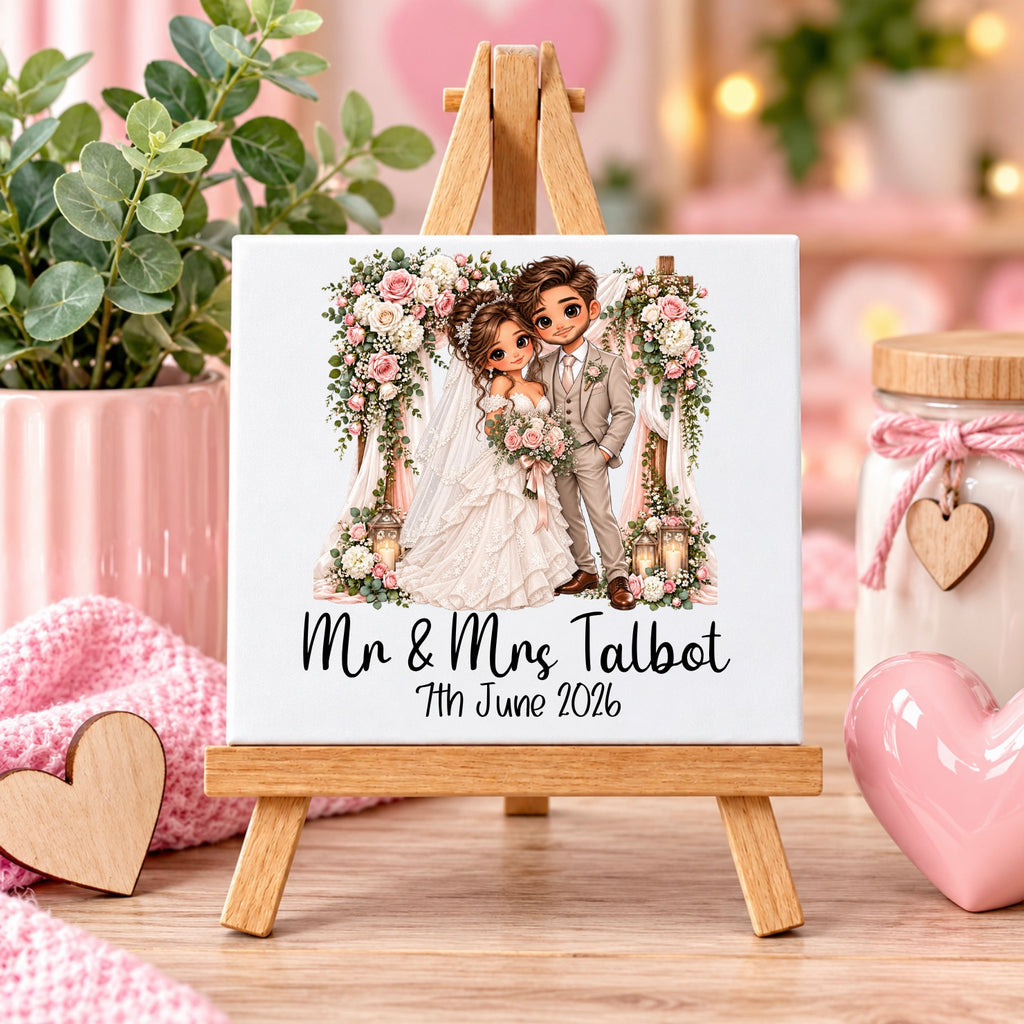 A personalized square canvas print showing a cartoon-style wedding couple under a floral arch, displayed on a small wooden easel. The text below reads 'Mr & Mrs Talbot 7th June 2026'.