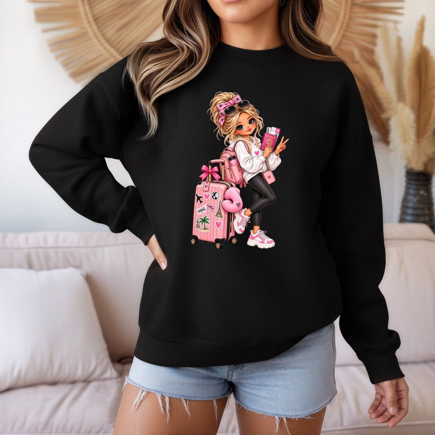 A woman wearing a black crewneck sweatshirt with a colorful cartoon graphic of a girl with pink hair and luggage, paired with light blue denim shorts in a living room setting.